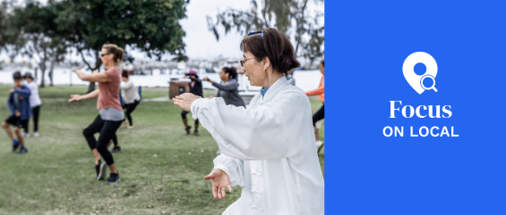 Chinese woman practicing tai chi with group of people outdoors