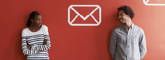 Two people stand in front of a red wall with email icons 