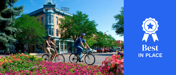 People on bikes ride past historic buildings and pink flowers in Downtown "Old Town" Fort Collins. 