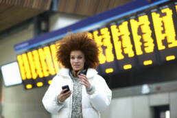 Young woman at train station, holding smartphone